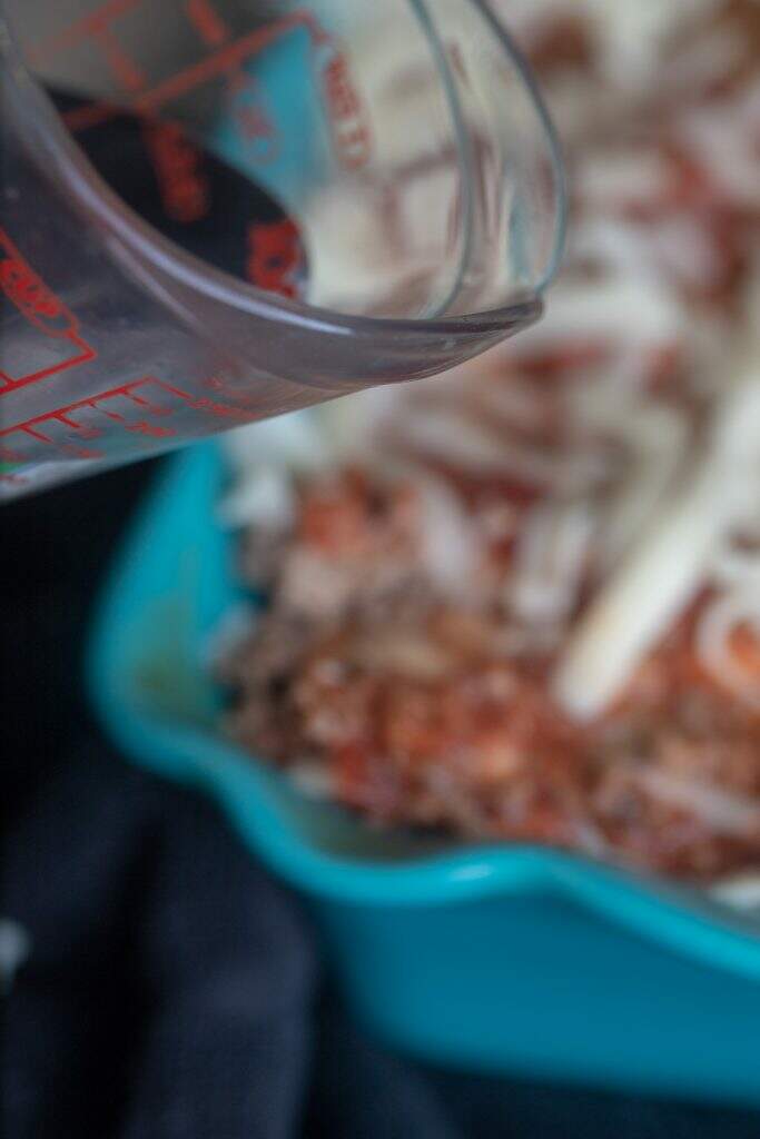 hot water being poured in casserole dish of easy homemade lasagna