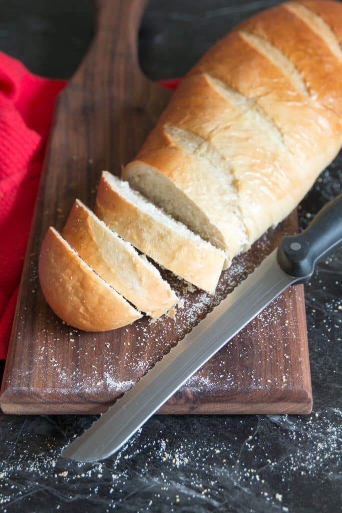 Soft french bread sliced on cutting board with knife