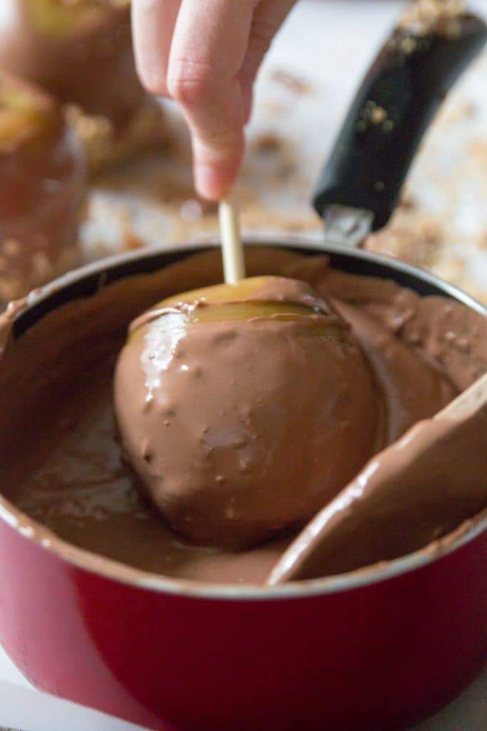 Homemade caramel apple being dipped in chocolate