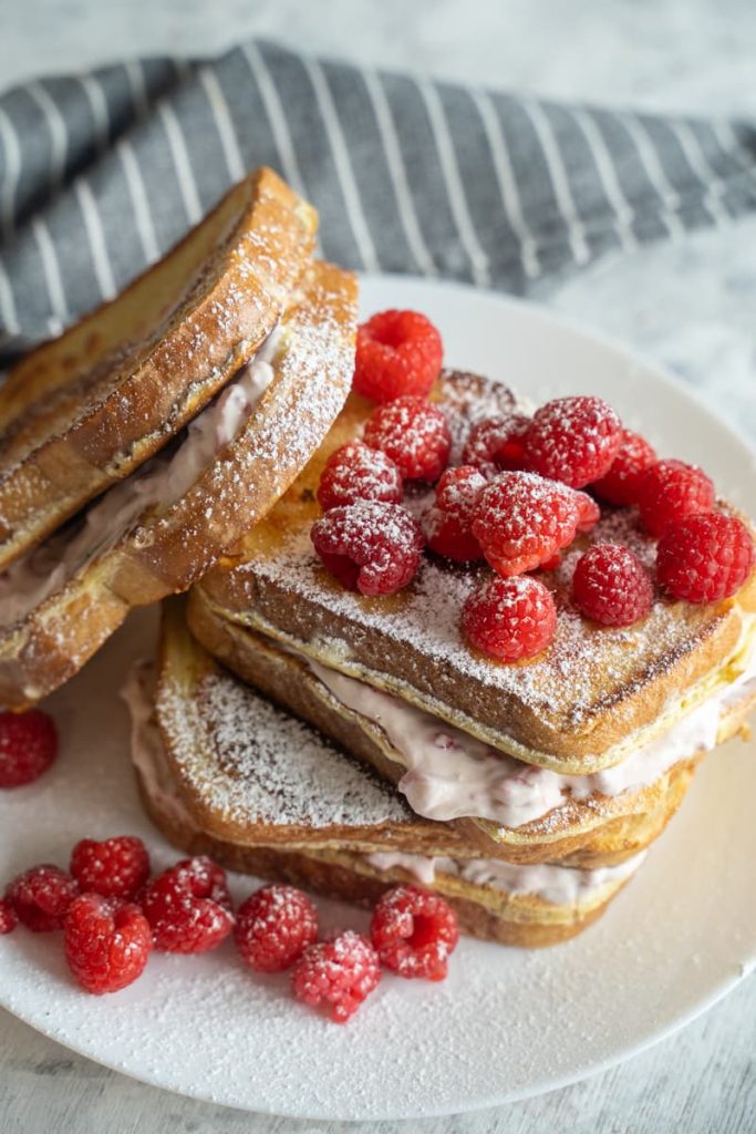 High Protein Raspberry Cheesecake stuffed french toast stacked with fresh raspberries on top and a grey napkin