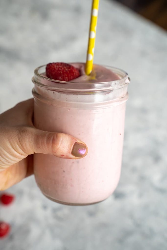 Hand holding pink starburst smoothie with yellow straw in a mason jar with white background