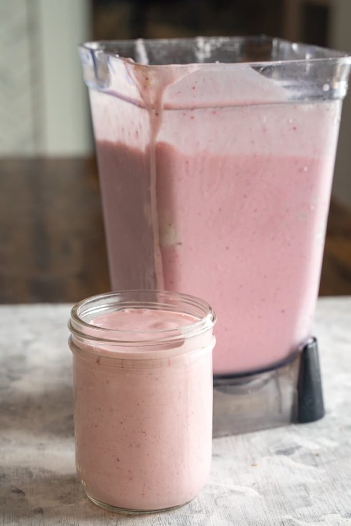 Full blender with healtheir pink star smoothie with mason jar in front with smoothie